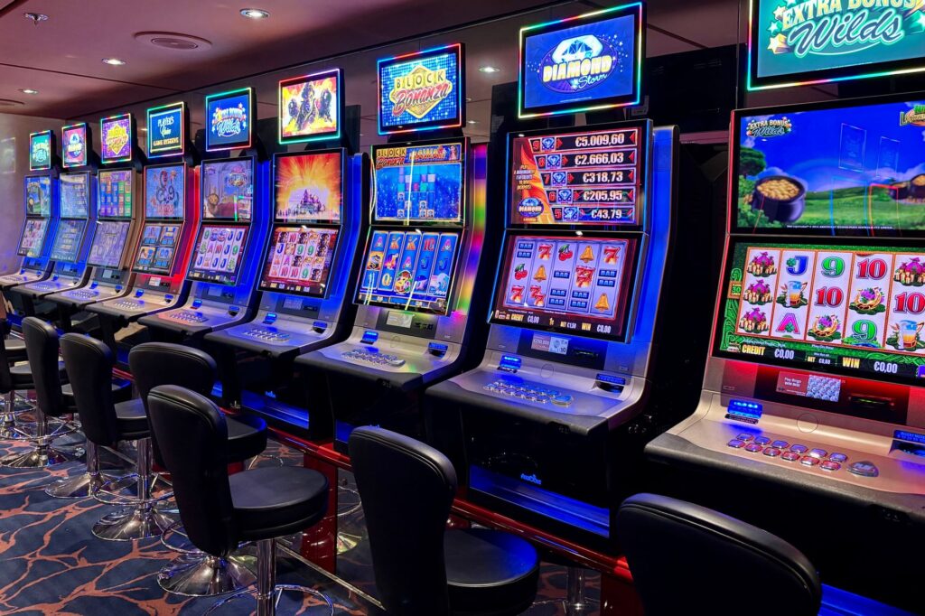 Row of glowing slot machines with empty chairs in dim casino
