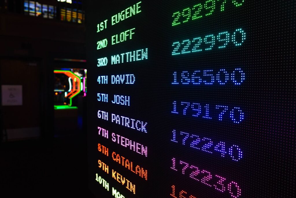 Neon leaderboard screen listing player names and scores in dark room